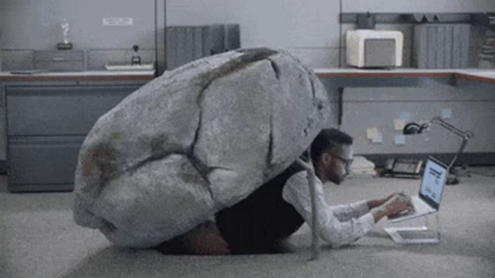 a man with a large rock on his back is using a laptop computer