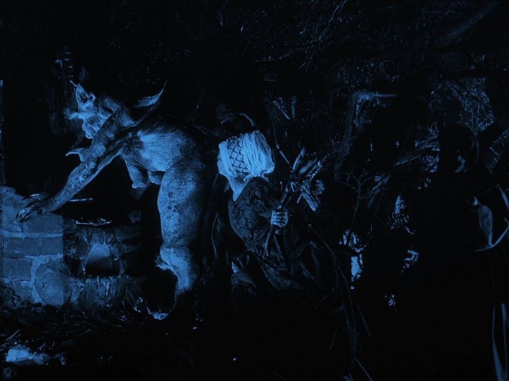 A scene from the 1922 horror-documentary Häxan where the initiation of witches is recreated for the edification of the audience. in a monochrome black-and-blue shot meant to evoke the deepest night in the darkest forest, a procession of elderly women in dark dresses line up to kiss a bent-over demon on their proffered rump. The demon leans with straight arms over a brick altar. They are very tall and full-figured, with bushy eyebrows, batlike ears, spiky joints, claws, and pendulous breasts. Another, taller devil watches from the darkness. The woman at the front of the line has her face buried in the plush cheek of evil, and everyone is having a nice time.