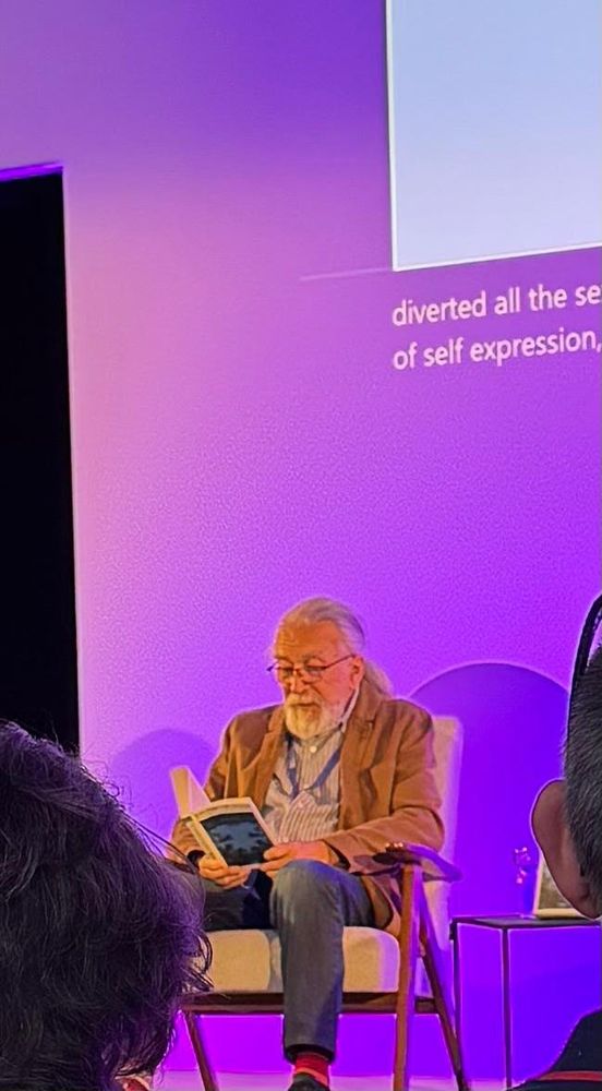 author reads from his 40 year old novel under the lights in Edinburgh. heads in foreground. 