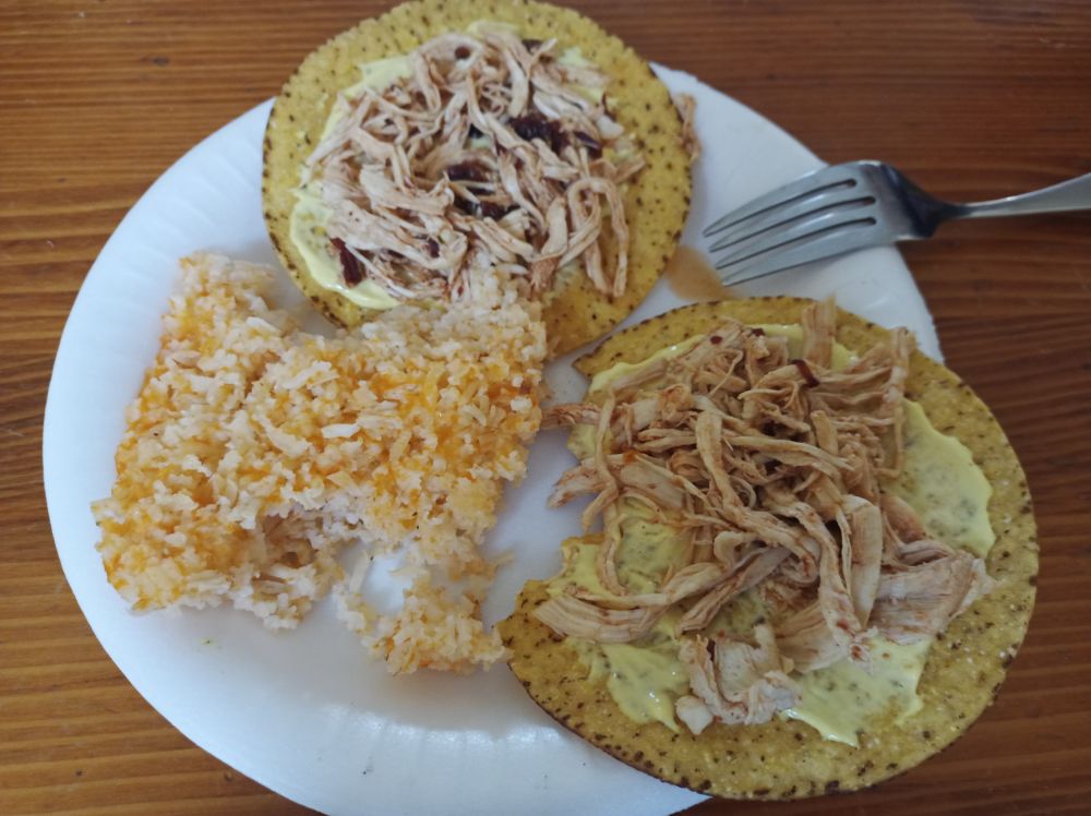 two chicken tinga tostadas and mexican rice on a foam plate with a fork laying on the edge of the plate