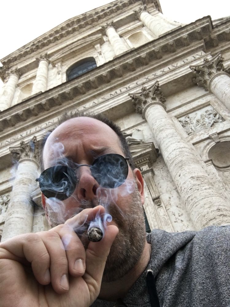 Person in sunglasses puffs a cigar on the streets of Rome 