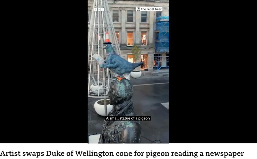 statue of a pigeon reading a newspaper while pooping on the head of the statue it's perched on