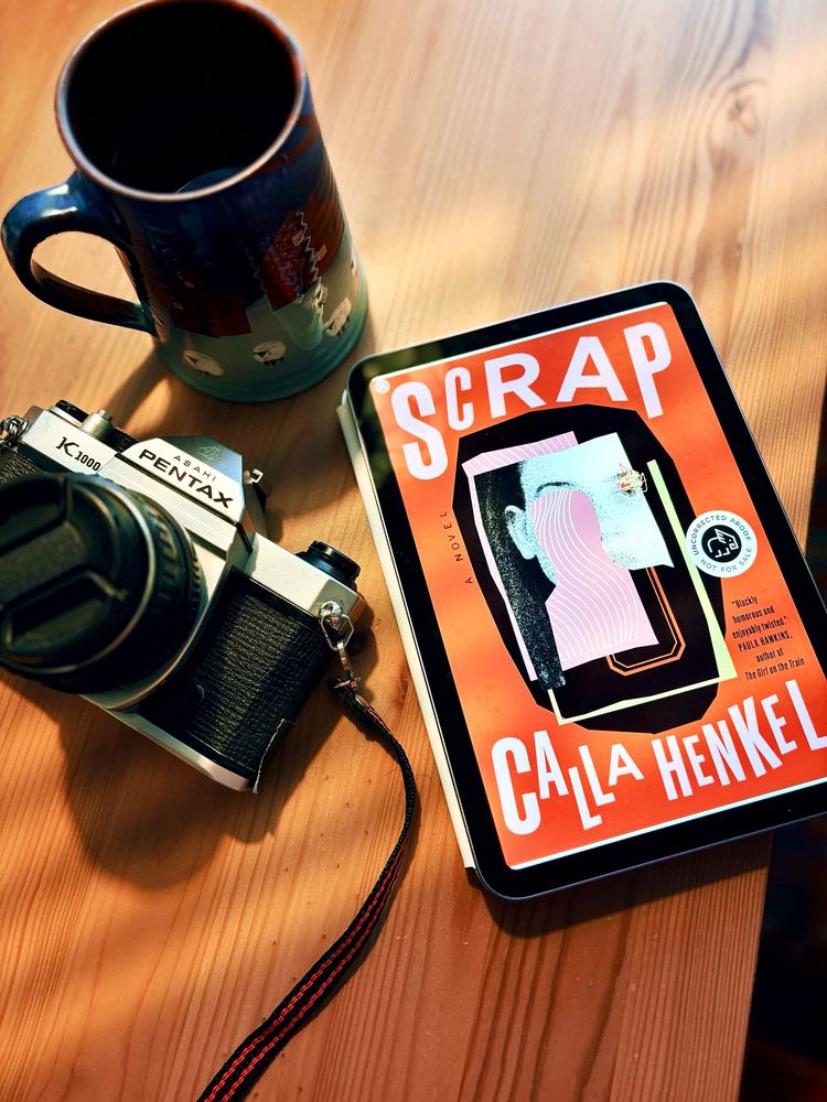 Scrap by Calla Henkel next to a cup of coffee and a Pentax camera.