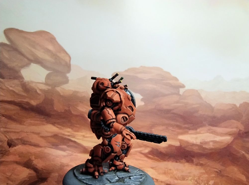 Miniature of a sci-fi armoured suit,
 painted orange in front of a background pictue of orange rocks