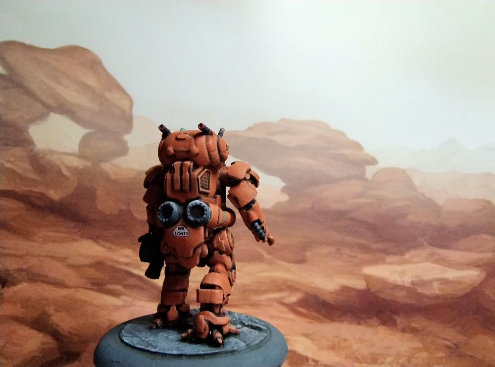 Miniature of a sci-fi armoured suit,
 painted orange in front of a background pictue of orange rocks