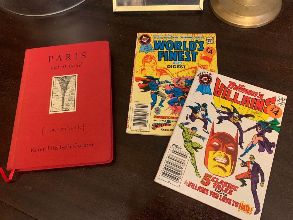 photo of Paris Out of Hand by Karen Elixzabeth Gordon (made to look like an old red Baedecker’s Guide Book) and two DC comics digests: World’s Finest and Batman’s Villains. 