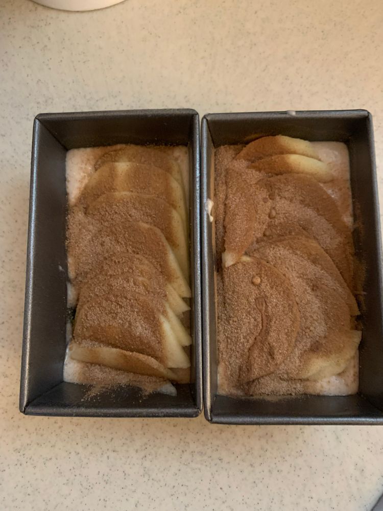 apple cider nuffin batter in two mini tins with a layer of sliced apple on top and too much cinnamon sugar 