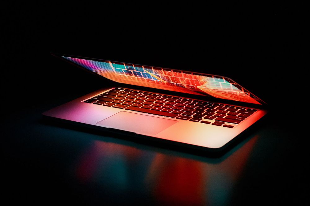 A laptop partially closed reflecting colorful light in a dark space
