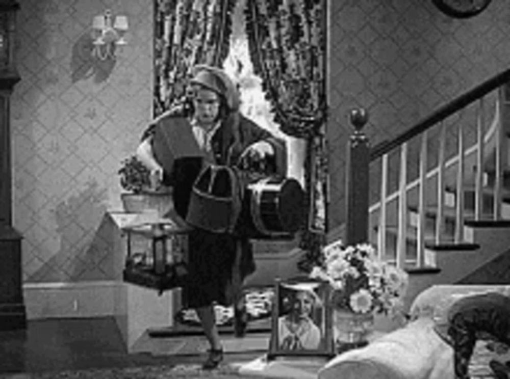 a black and white photo of a woman standing in a living room holding a birdcage .