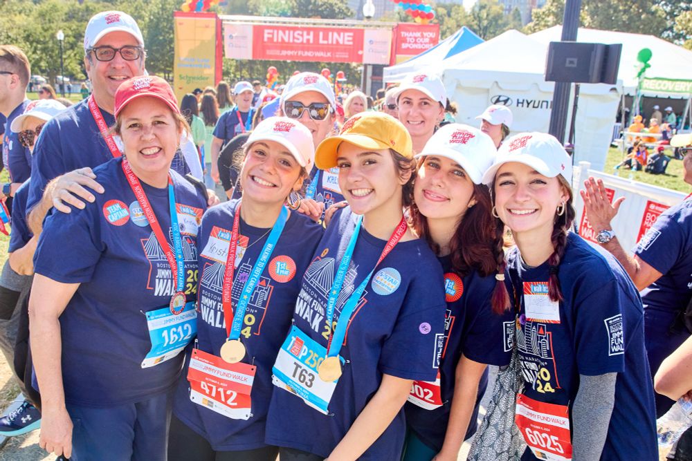 A group of Jimmy Fund Walk participants smile together with the finish line in the background.