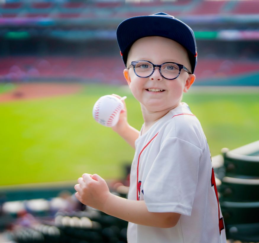Owen smiles while preparing to throw a baseball. Behind him is the outfield of Fenway Park, home of the Boston Red Sox and longtime partner of the Jimmy Fund.