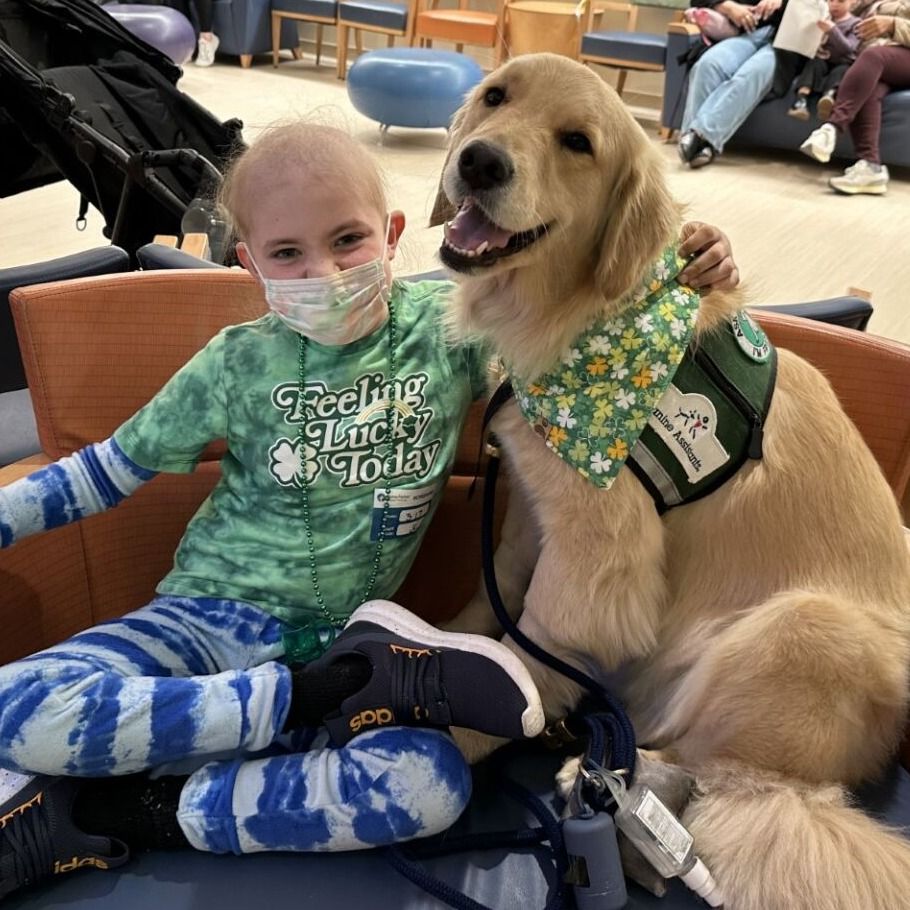 Finn wears a mask in Dana-Farber’s the Jimmy Fund Clinic with his arm around Opry, the Pediatric Facility Dog.