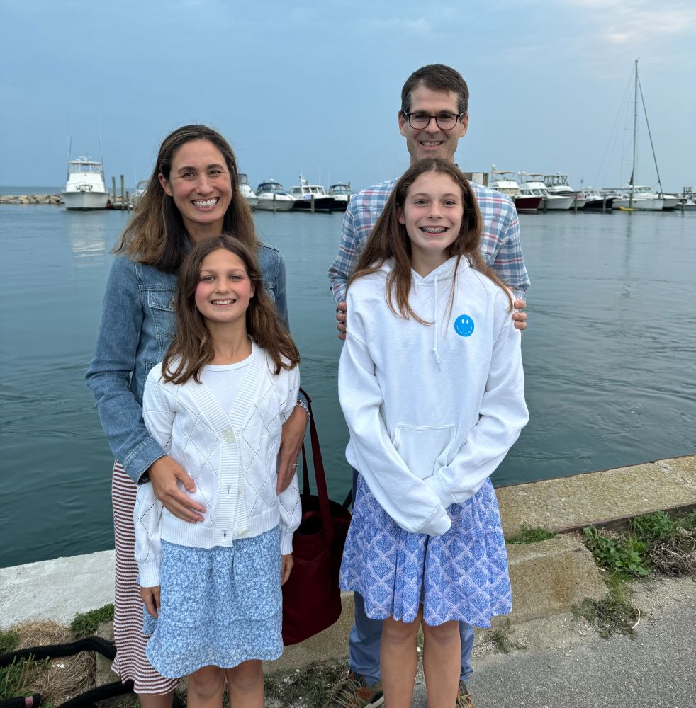 Catie stands by the ocean with her husband and two daughters.