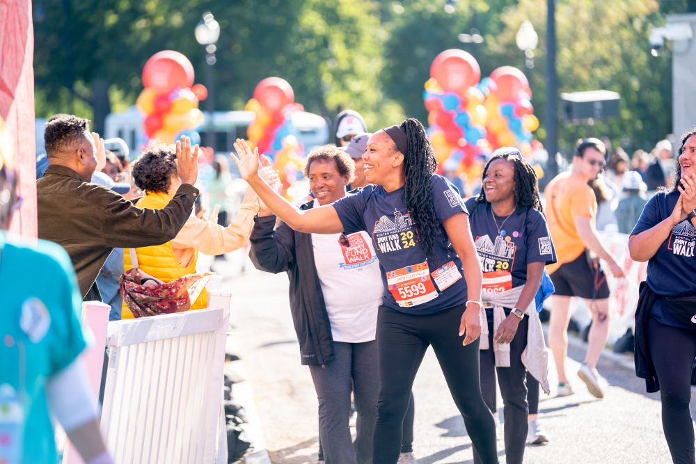 A Jimmy Fund Walk participant gives a high-five to a spectator while on the course.