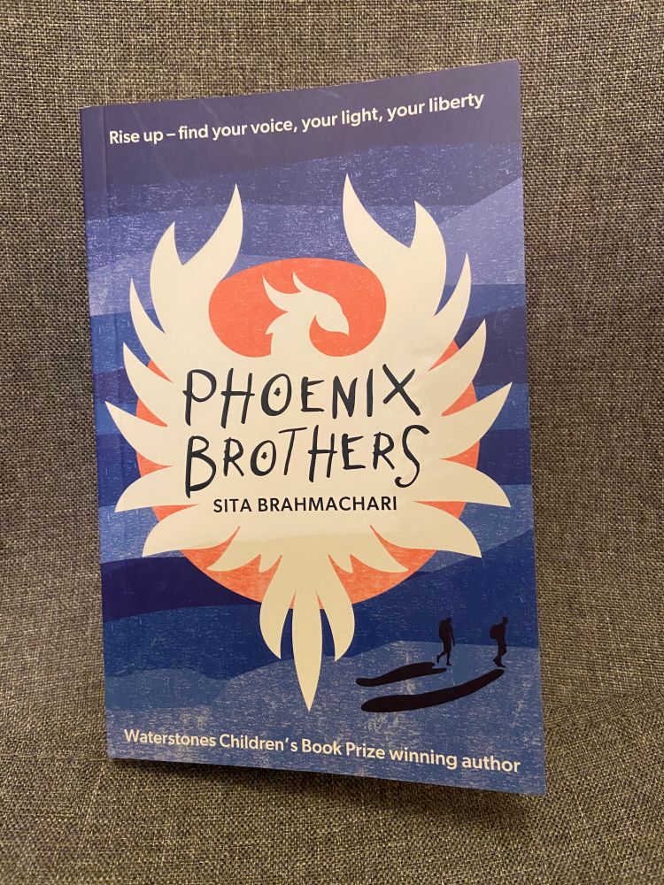 The book cover for Phoenix Brothers by Sita Brahmachari has the words Rise up - find your voice, your light, your liberty - across the top. The title and author's name is in the white silhouette of a phoenix against an orange sun. There is a blue background in rows, like waves and the silhouettes of two figures in the bottom right hand corner. They are carrying backpacks and casting long shadows.