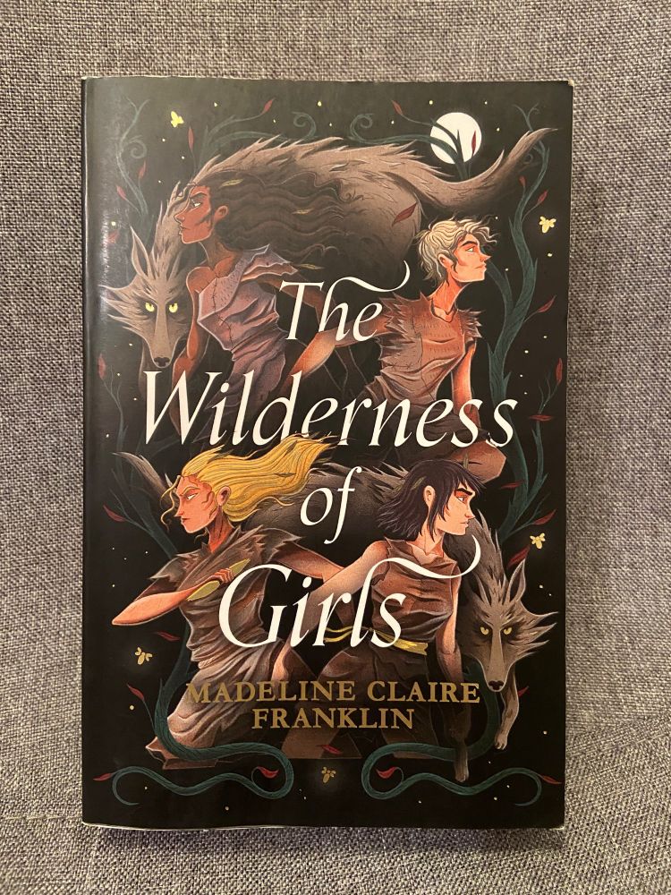 The book cover for The Wilderness Of Girls by Madeline Claire Franklin is an illustration of four wild looking girls looking out to each of the 4 edges of the book with 2 wolves, one at the top left and one on the bottom left. The title is in the centre in white lettering with the author's name underneath in gold lettering. The background is black.