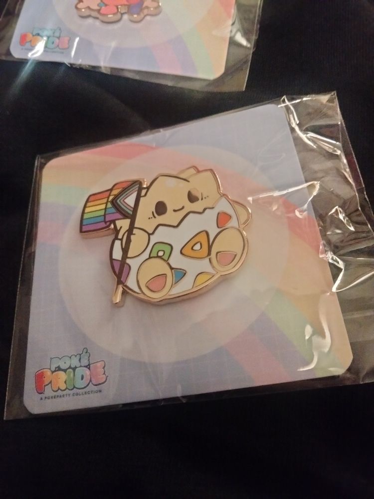 A pin of a Togepi holding a pride flag while smiling. 