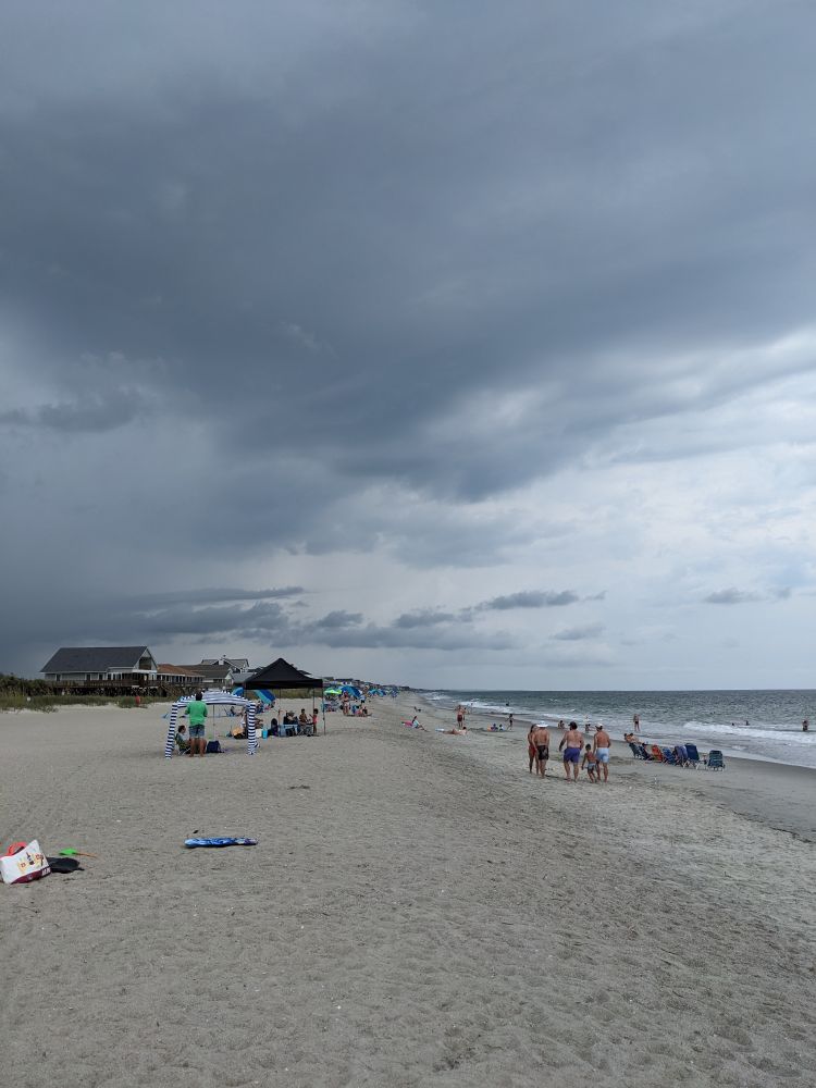A long sandy beach with dark storm clouds looming above it.