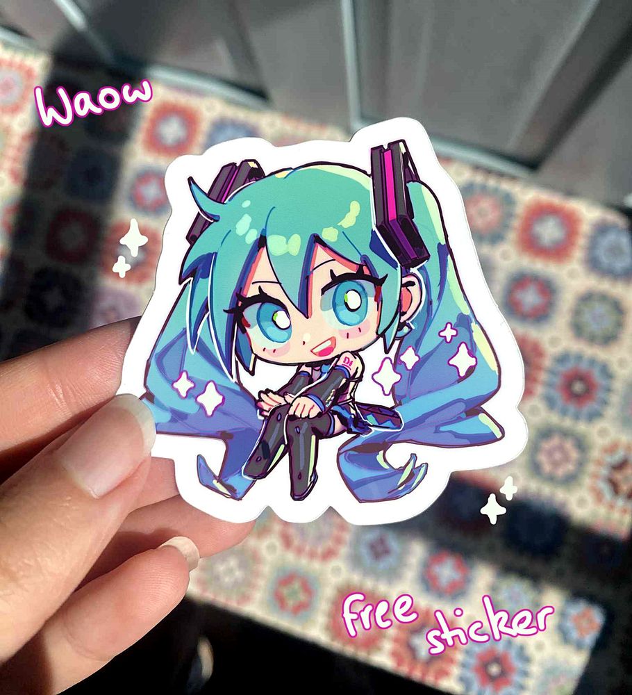 A hand holding a chibi illustration sticker of Hatsune Miku. She is smiling brightly, sitting and kicking her knees. The art is adorned with sparkles. The words "waow, free sticker" are written on either side of the image.