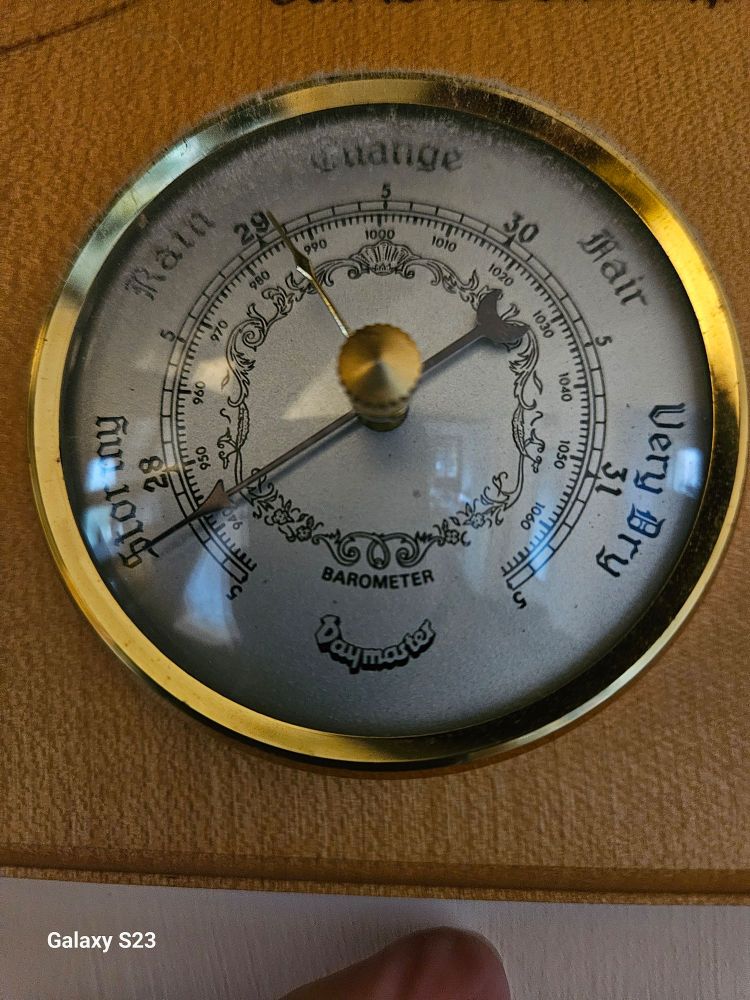 Photo of cheap, old, barometer with needle pointing to the S of Stormy indicating very low pressure.