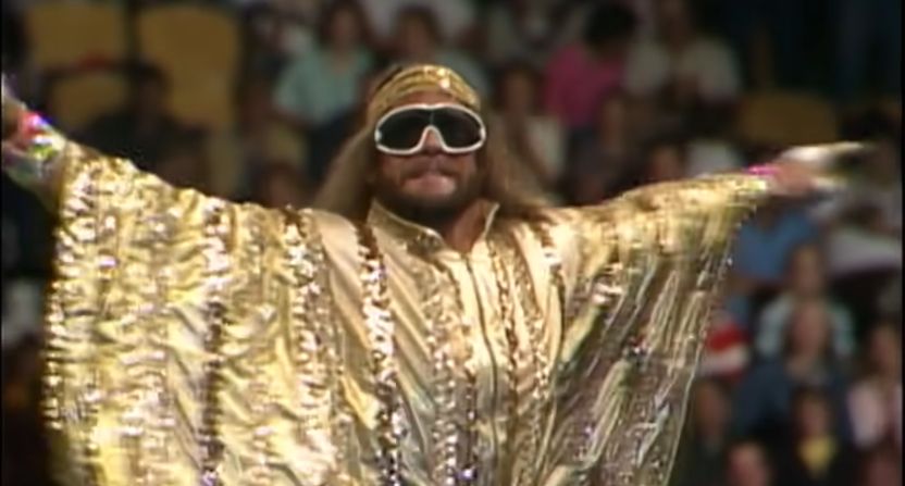 “Macho Man” Randy Savage, wearing massive sunglasses and golden robe as he spreads his arms to show it off.