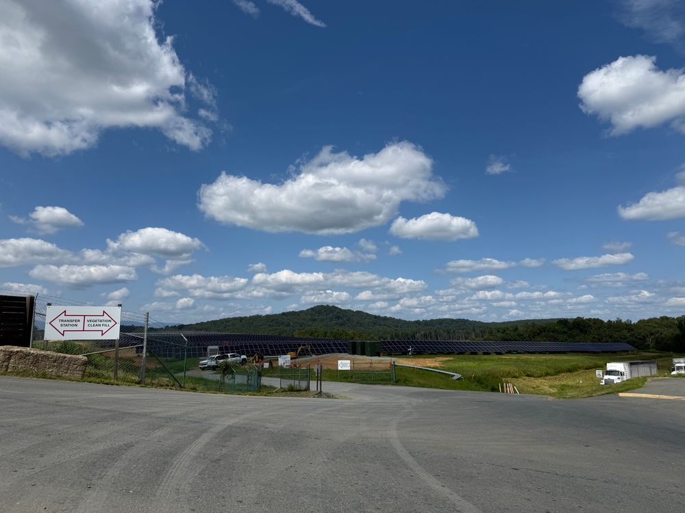 Lots of solar panels in a field with a blue sky with white clouds and a mountain