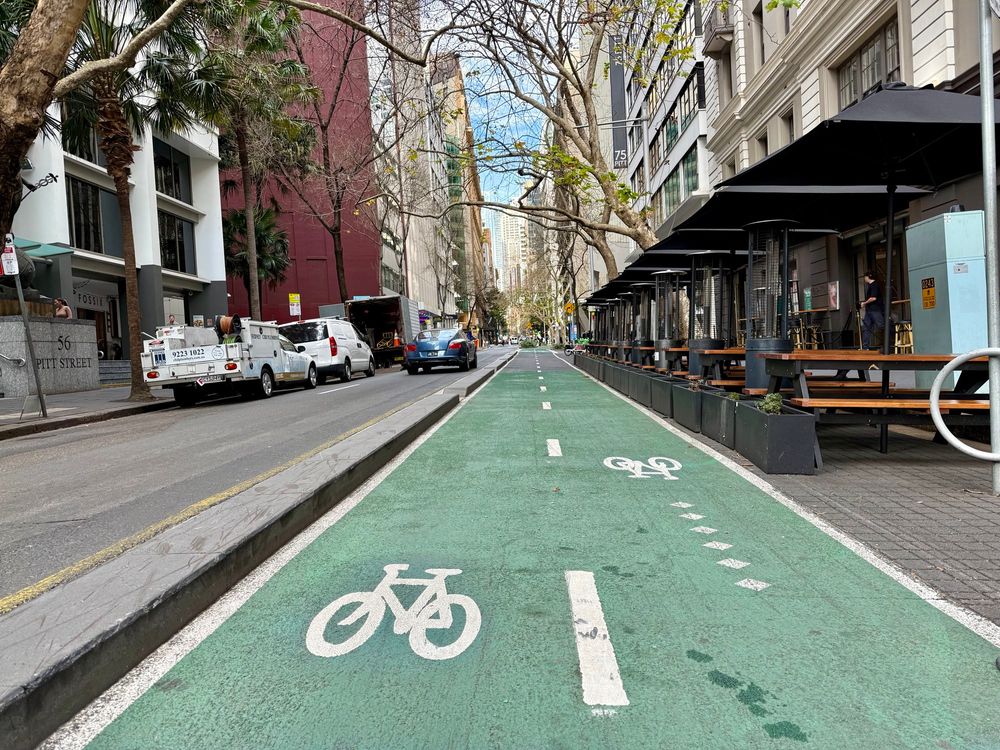 Lane cars, lane for parking, protected bike lane - actual protection - bi-directional bike path painted green, wide sidewalk with tables for eating, and walking
