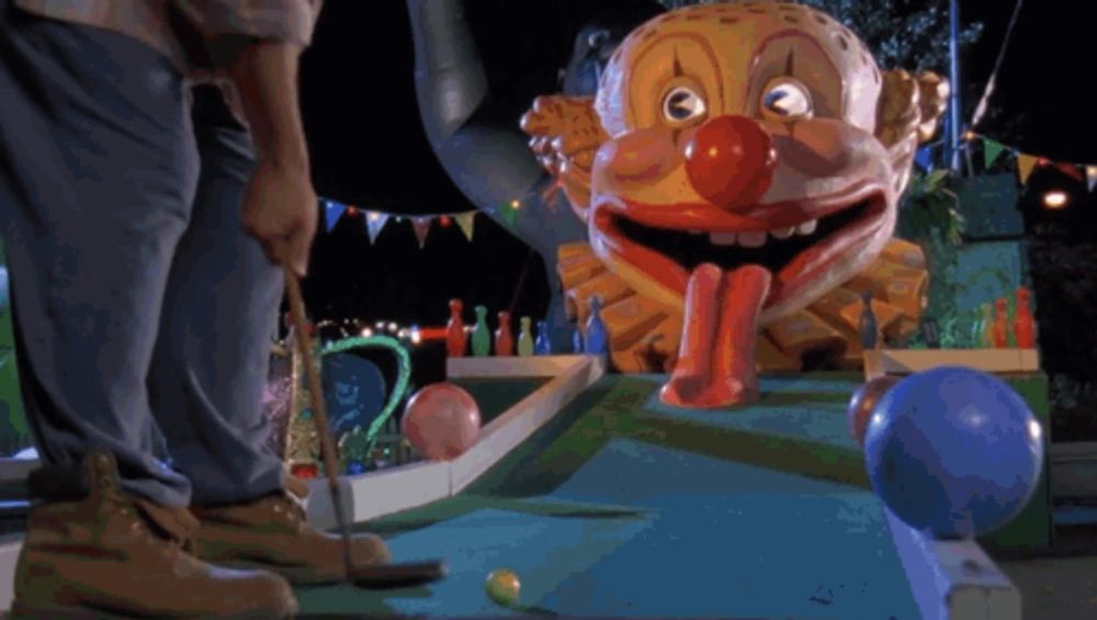 a man is playing a game of mini golf with a clown head in the background