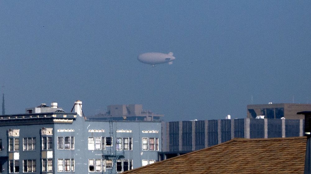 A large white blimp in the sky above downtown San Francisco, CA.