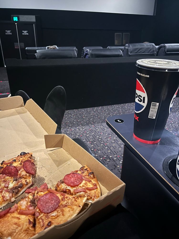 Pizza in lap , sitting in recliner facing theatre screen before movie starts 