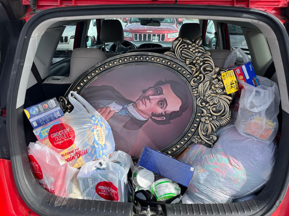 A decorative portrait of Master Gracey from Disney’s Haunted Mansion rests in a car trunk among bags of groceries.