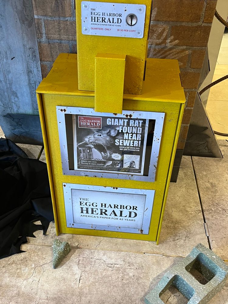 A display of a newspaper machine featuring Egg Harbor Herald, an Easter egg pointing to the Spirit Halloween flagship store. There’s a front page story about giant mutant rats invading the sewer.