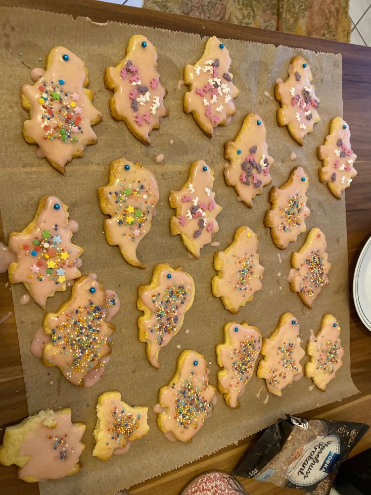 Fertig gebackene Dinosaurier Plätzchen verteilt auf einem Backpapier mit rosa Zuckerguss und verschiedenen bunten Streuseln drauf