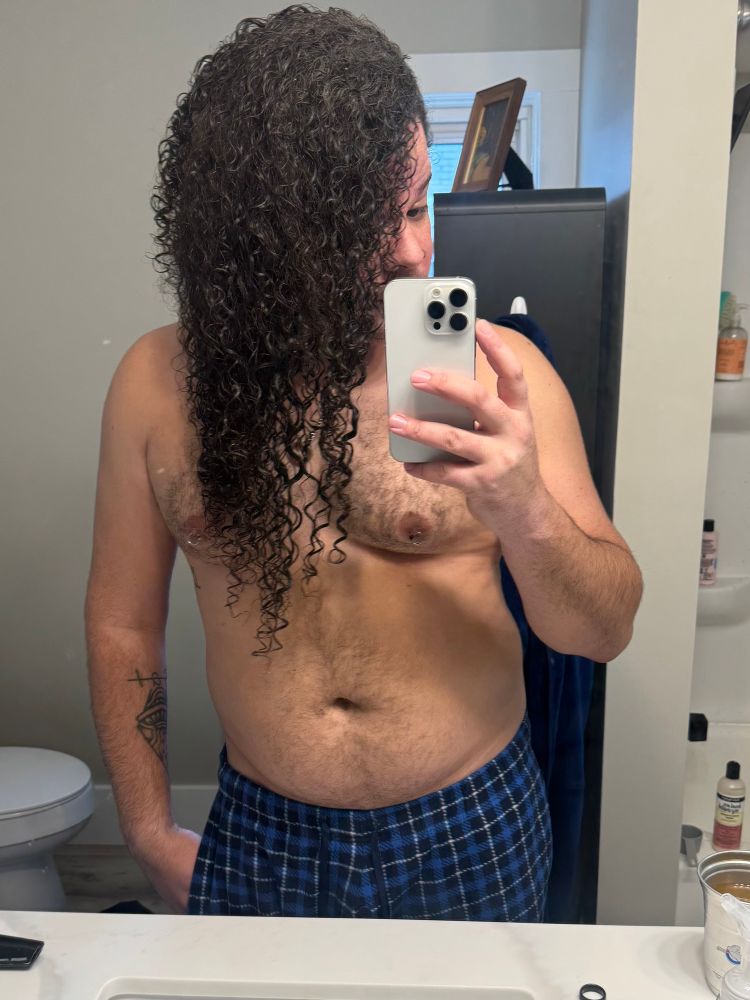 photo of Ghost in the bathroom mirror shirtless with wet hair (mid-detangling) and blue pajama pants on