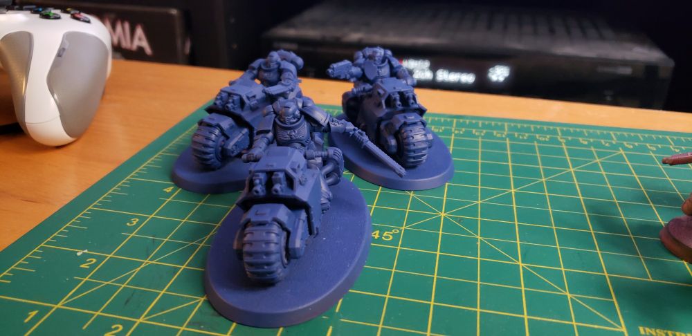 A photo of some Warhammer 40,000 models. There are three space marines on motorcycles, referred to as an Outrider Squad. They have been sprayed with a blur base coat but are otherwise unpainted.