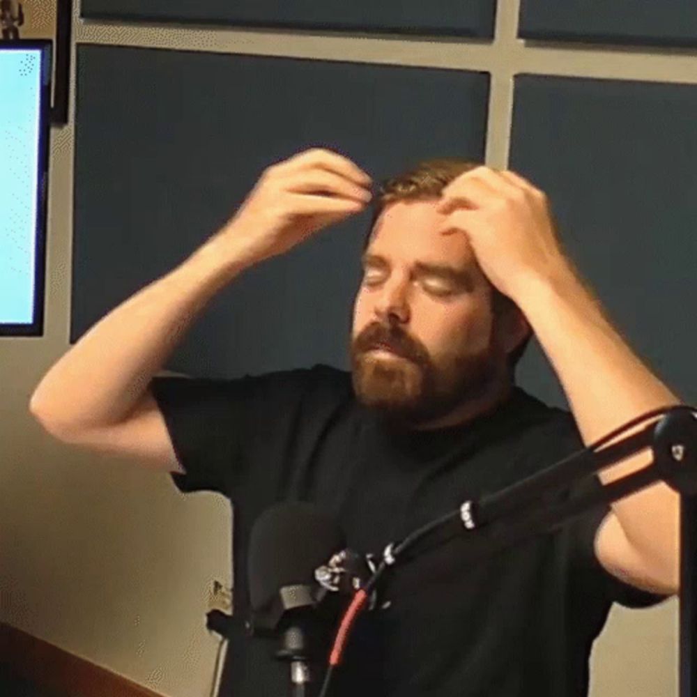 a man with a beard is standing in front of a microphone and adjusting his hair