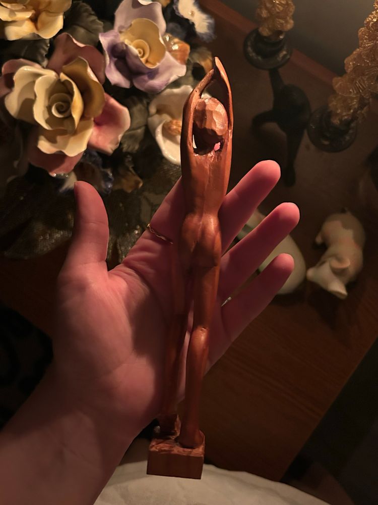 A wooden carving of a feminine figure viewed from the back 