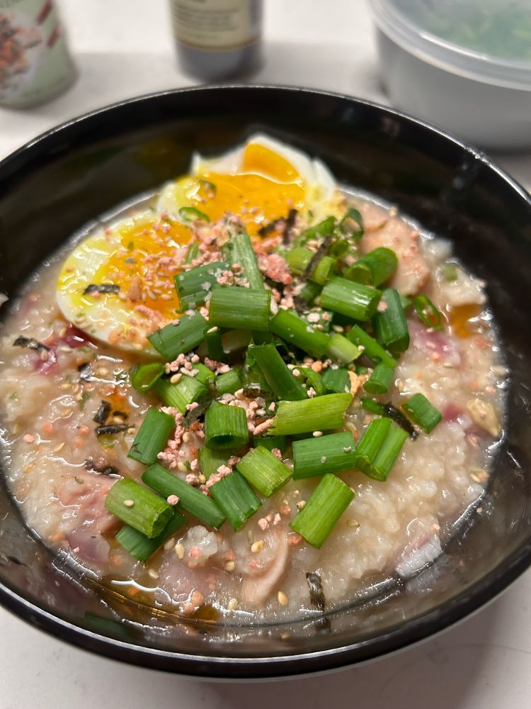 A bowl of chicken congee with soft boiled egg, green onions, and furikake 