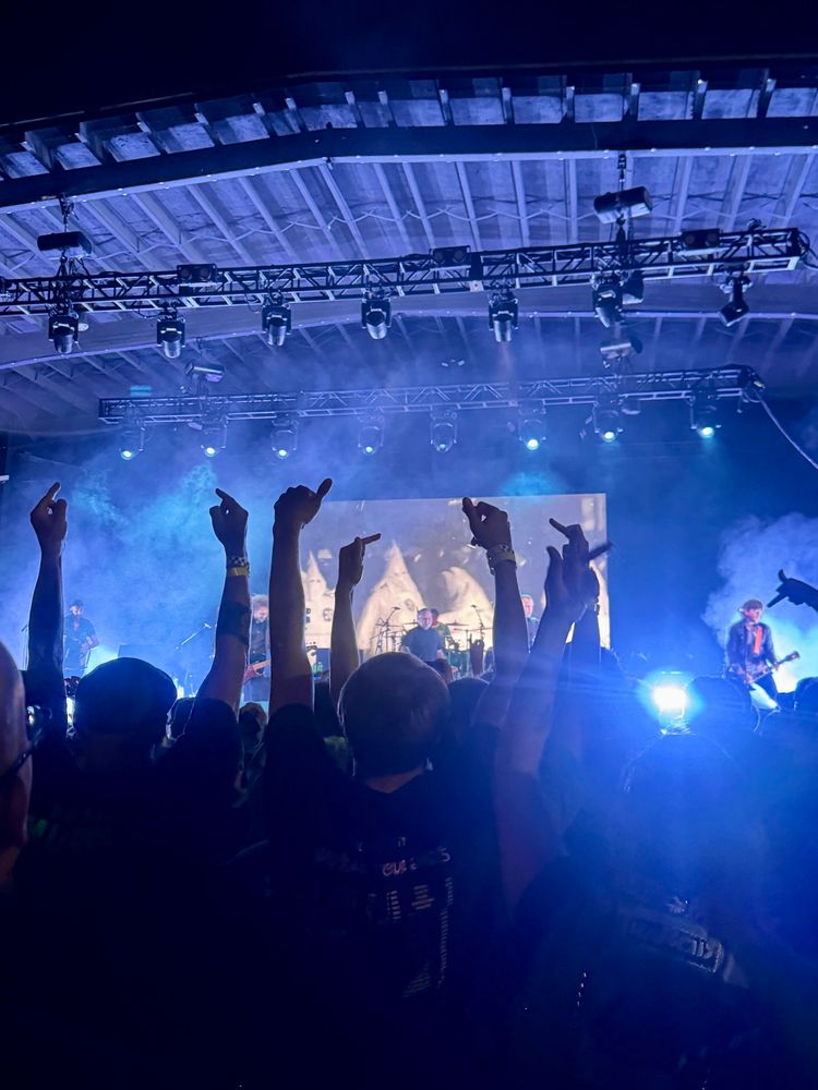 A photo taken of the stage during a Dropkick Murphys show. The backdrop video shows members of the KKK marching, and the crowd’s arms are raised at the screen, middle fingers high. 