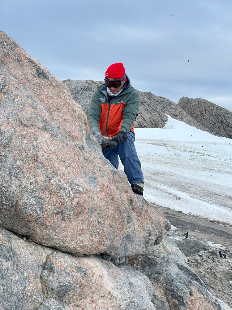 Geologist sampling rocks with snow and penguins in the background 