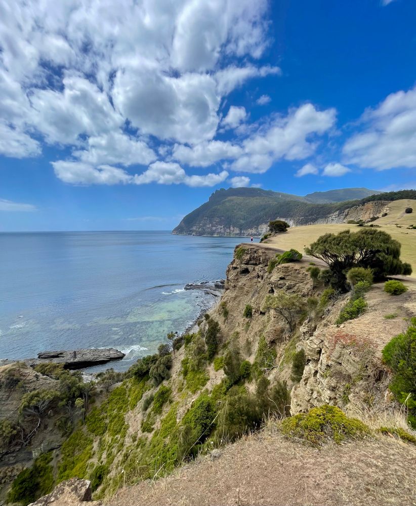 Sandstone cliffs by the sea with mountain peak in the background 
