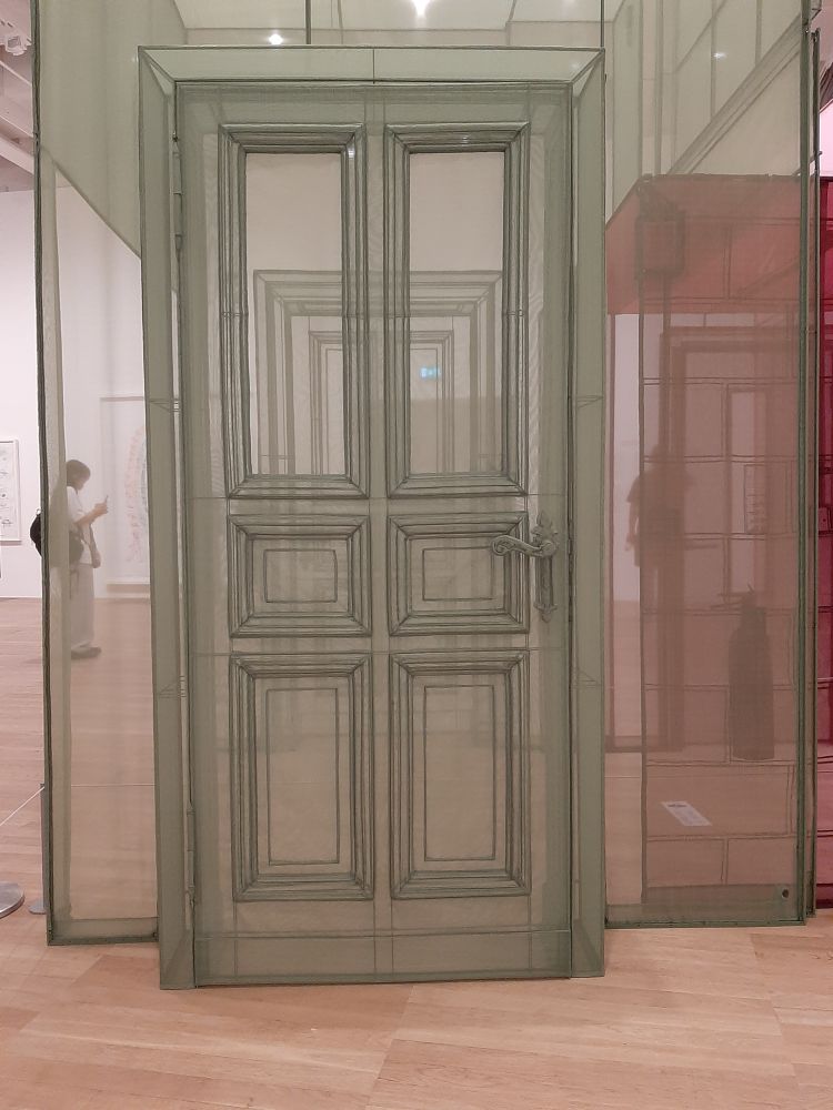 A life-sized representation of a panelled door made of olive green nylon gauze