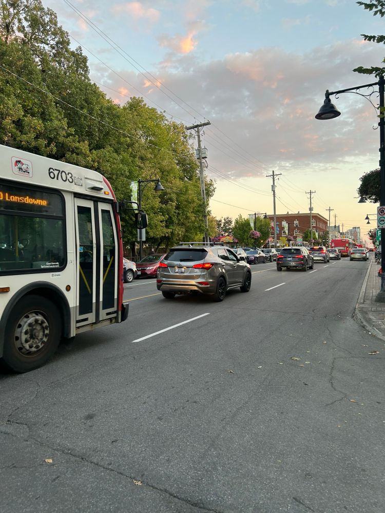 Traffic backed up on Bank Street headed towards Landsdowne. The left hand lane is bumper to bumper while in the right hand lane there are two parked cars.