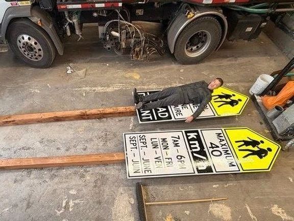 A person lying on large road signs positioned on the ground, next to a truck.