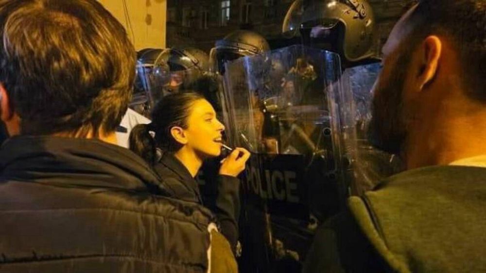 A protester applies lipstick in the reflection of a riot shield.