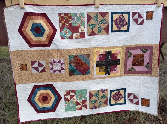 Comfort quilt made in 3 columns featuring two large hexagon blocks. Outer columns' blocks are small at the top of the quilt and get larger going down. Center column is the opposite. Blocks are made of fabric in autumnal colors: green, rust, gold, brown and touches of pink.