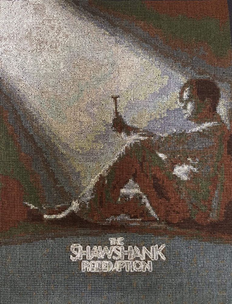 Cross stitch of man holding a small hammer in a beam of light