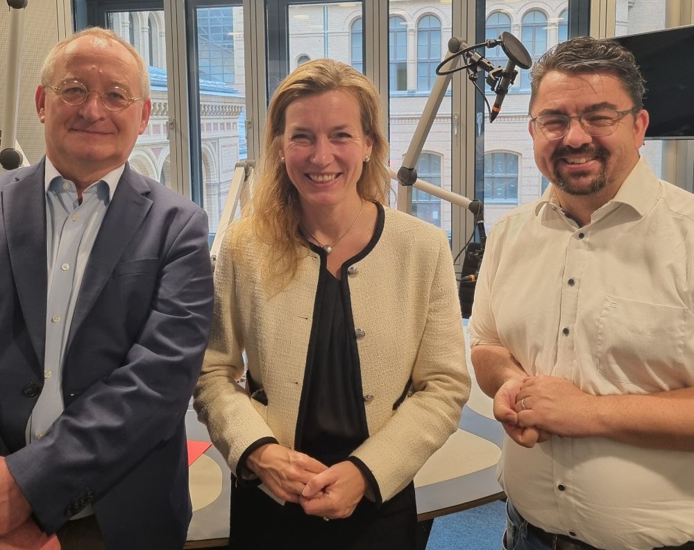 (von links) Erhard Scherfer, Siemtje Möller und Thorsten Faas im Hörfunkstudio und fröhlich in die Kamera blickend. 