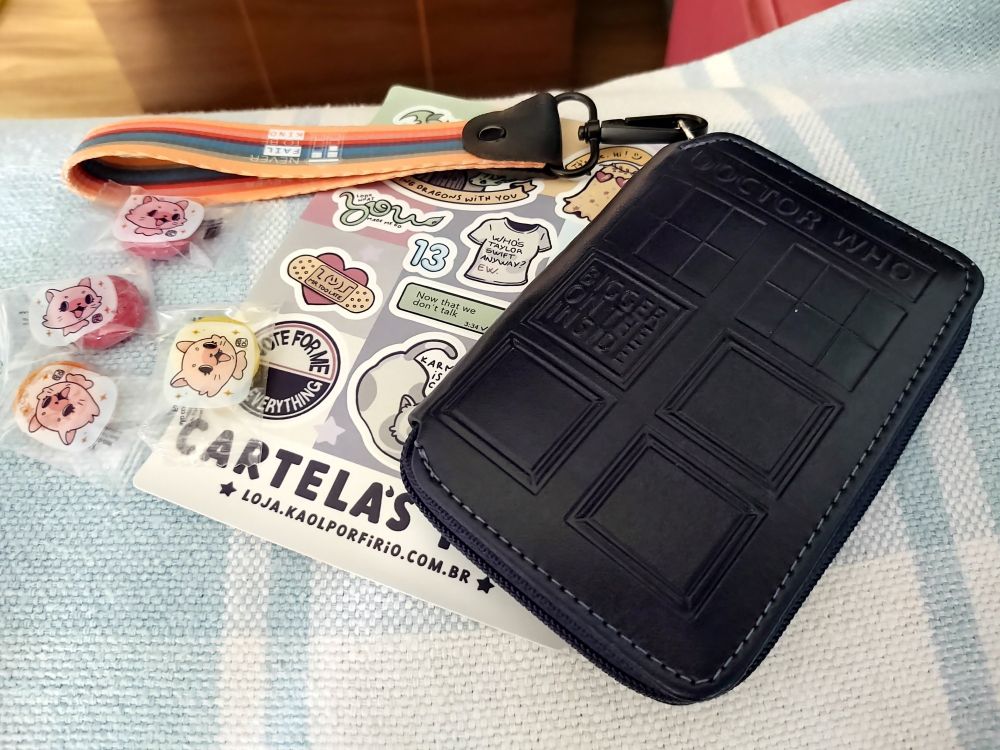 Foto de uma carteira no formato da porta da TARDIS, uma cartela de adesivos baseados em músicas da Taylor Swift e quatro balas estilo bala soft 