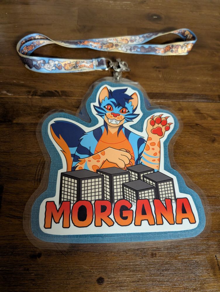 A laminated badges showing a bust of Morgana, a blue and orange monster cat, towering over some skyscrapers 